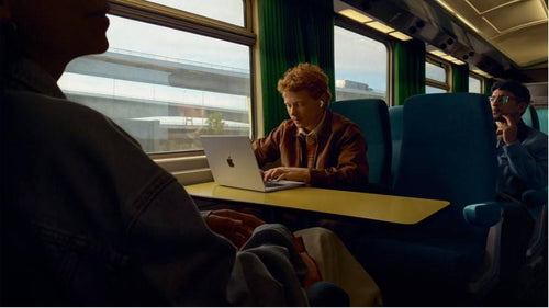 Una hombre usando sus AirPods con una Macbook en un tren. 